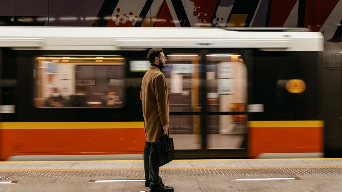 A man in a coat holding a briefcase stands at a train station platform as a train passes by.